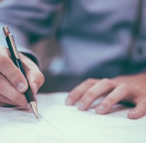 Hand signing a legal document with a pen on a desk