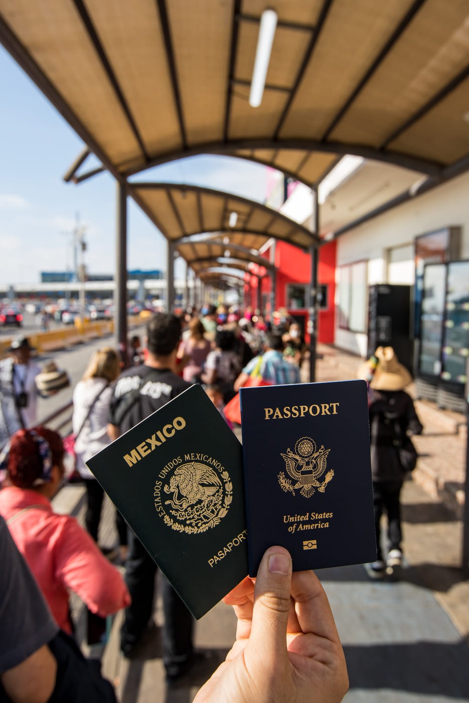 A hand holding a Mexican passport and a United States passport at a pedestrian border crossing.
